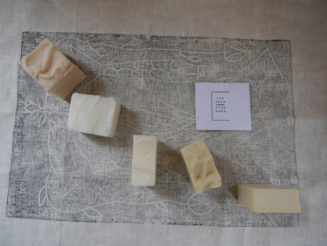 Five functional soap bars spread out on a linen cloth with a lino print First Nations design