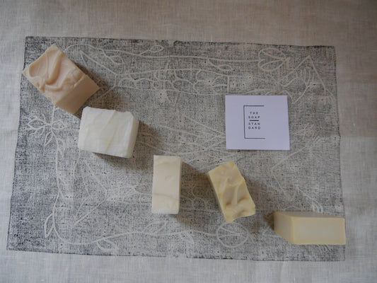 Five functional soap bars spread out on a linen cloth with a lino print First Nations design
