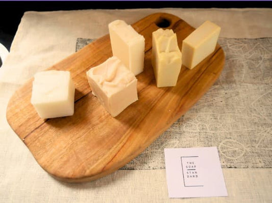 5 uniquely textured soap bars on top of a wooden chopping board and linen cloth printed with First Nations lino art.