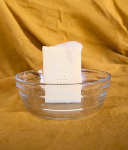 Light yellow soap bar in a clear glass bowl with suds on top. Yellow background